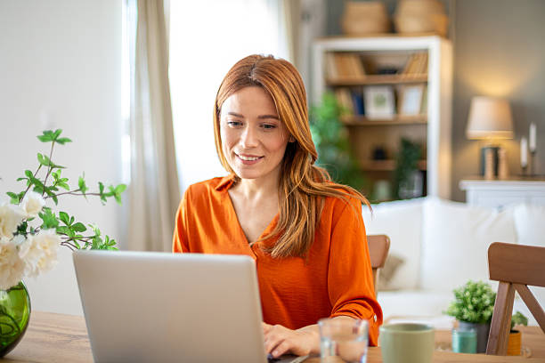 istock Smiling woman working from home on laptop at dining table 2211784706