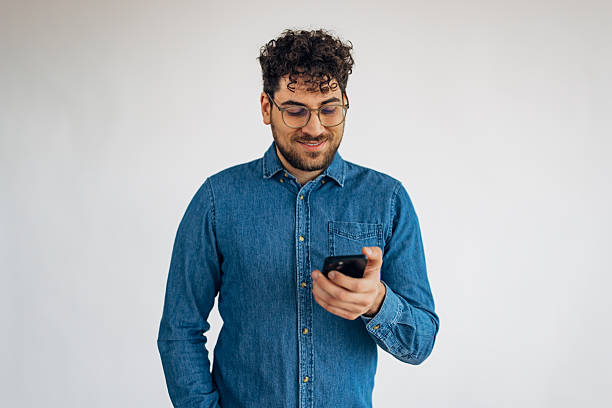 istock Front view of smiling man standing in front of white background and using smartphone to communicate with friends 2211793121