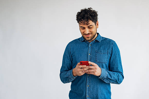 istock Front view of handsome man standing in front of white background and using smartphone to communicate with friends 2211793401