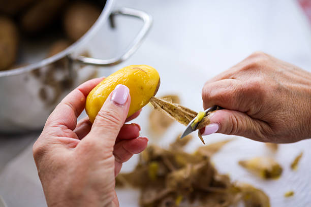 Woman peeling jacket potatoes in their skin.