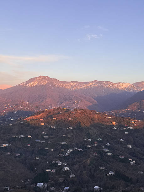 istock Mountain landscape with scattered houses on forested hills during sunset. Snow is visible on the higher peaks. The sky is mostly clear with light clouds. 2211800863