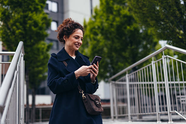 istock Smiling businesswoman using smartphone while walking in the city 2211808507