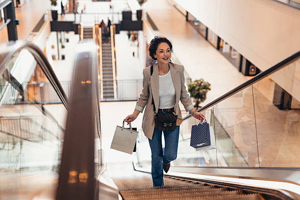 istock Happy customer going up the escalator with shopping bags 2211808839
