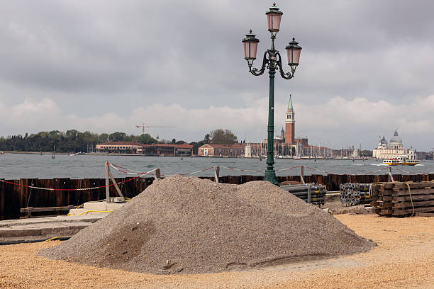 Construction materials and gravel on Venetian waterfront during infrastructure renovation works near the lagoon.