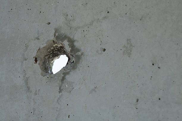 A concrete wall features a large hole revealing a brighter area behind it. The rough surface shows cracks and imperfections, suggesting wear over time.