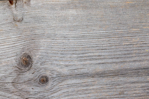 Close-up of weathered, gray-toned wood with prominent horizontal grain patterns and three knots. The wood surface displays cracks and texture.