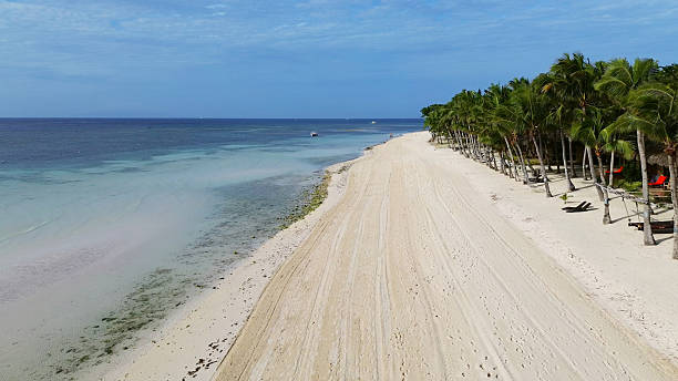 A couple strolls along the white sandy shores of a tropical island, surrounded by turquoise waters and lush greenery. A boat rests nearby, enhancing the peaceful island ambiance.