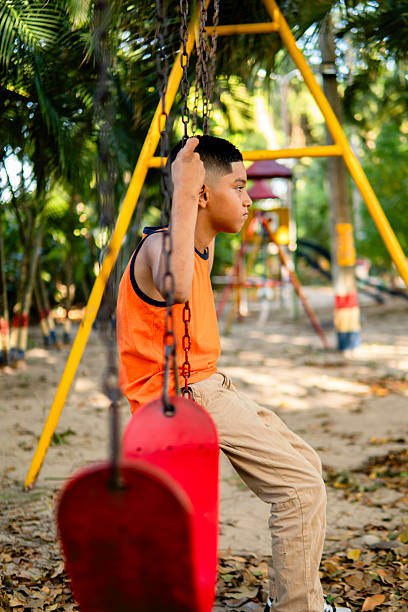 Child playing on outdoor playground in rain. Kids play on school or kindergarten yard. Active kid on colorful swing. Healthy summer activity for children in rainy weather. Little boy swinging.