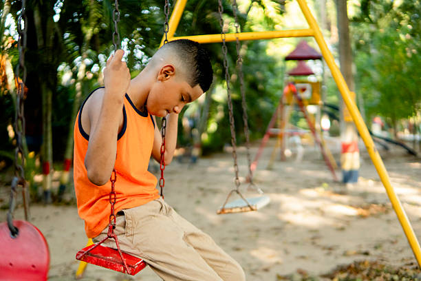 istock Sad child sitting alone on a swing in the playground feeling lonely 2211829204