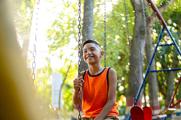 Portrait of a cheerful elementary age boy enjoying his time on a swing in a park, expressing happiness and carefree attitude