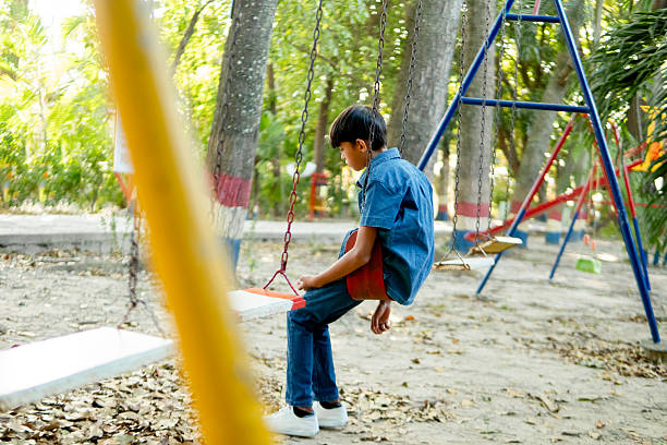 Lovely little boy smiling at the camera while playing on a swing set in playground joyfully
