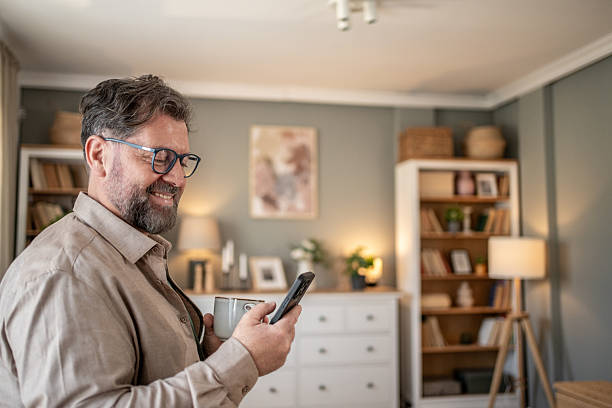 istock Smiling mature man enjoying coffee and using smartphone at home 2211833104