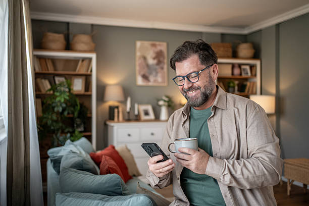 istock Smiling mature man using smartphone and drinking coffee at home 2211833314
