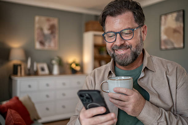istock Smiling mature man using smartphone and drinking coffee at home 2211833354