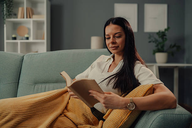 istock Young woman reading a book on the sofa at home 2211835714