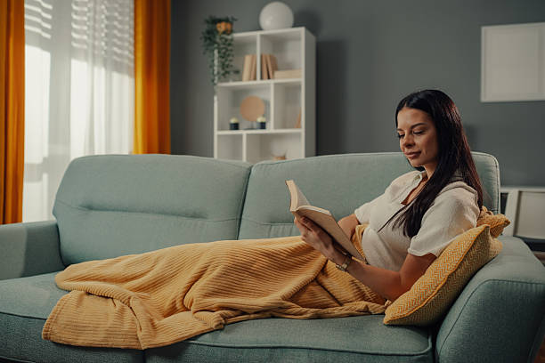 istock Young woman relaxing on sofa reading a book at home 2211835747