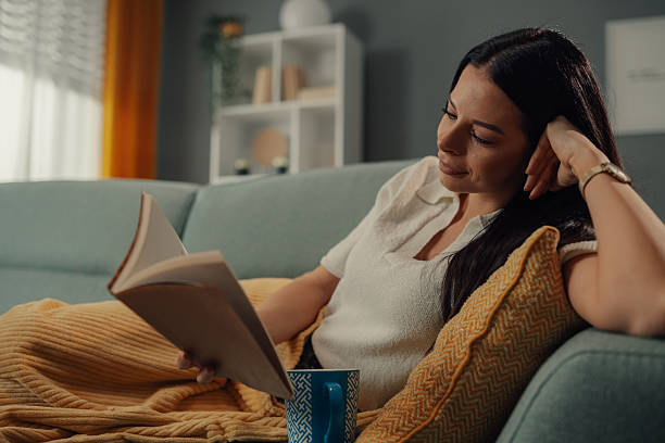 istock Young woman relaxing on sofa reading a book and drinking tea 2211835755