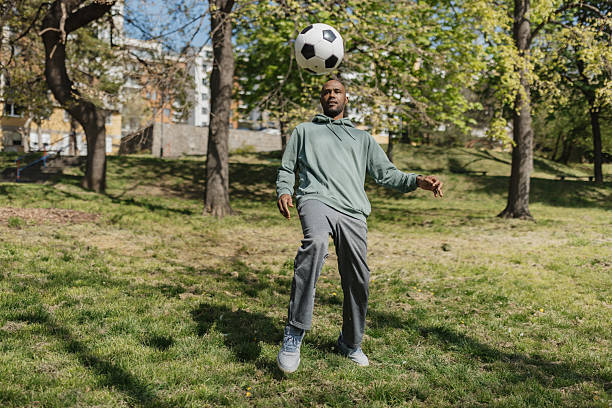 A man captures an exciting moment while balancing a bouncing soccer ball in a park, exuding energy and passion for the sport amidst a beautiful outdoor scene.