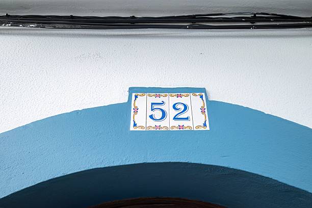 istock Traditional Portuguese Ceramic House Number Tile on Mediterranean Architecture. Decorative Blue and White Azulejo House Number 52 with Ornate Floral Pattern on Light Blue Arched Doorway Entrance in Azores Islands 2211839021