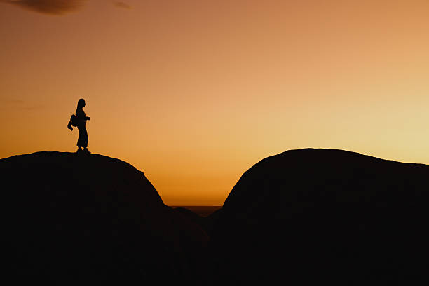 Silhouette of a hiker standing on a mountain peak, enjoying a breathtaking sunset