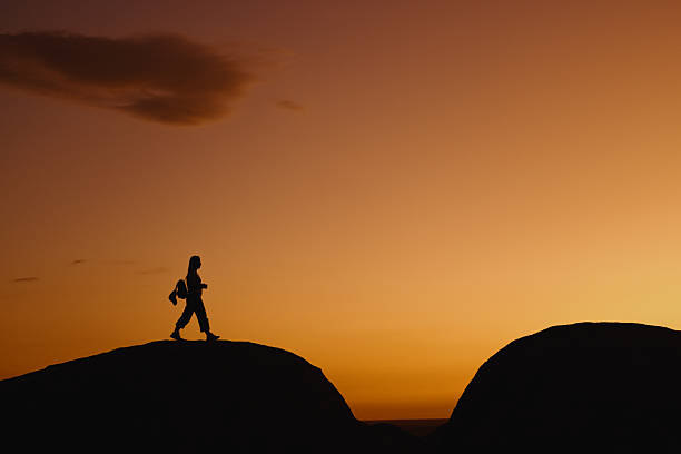 Silhouette of a female hiker walking on a rock formation at sunset, enjoying the beautiful view