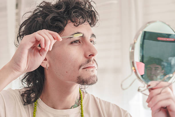 istock Young man combing eyebrows with a small brush and mirror in bathroom 2211847689