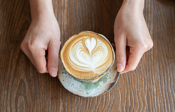Someone hands holding a cup of hot Cappuccino coffee before drinking.
