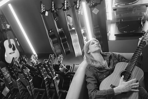 High angle black and white shot of mid adult female music store owner playing guitar after working day among neon lights in the evening
