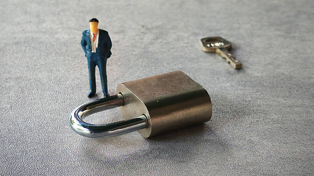 istock miniature businessman standing beside metallic padlock 2211869484