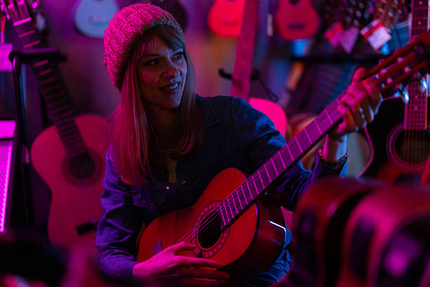 Mid adult female music store owner playing guitar after working day among neon lights in the evening