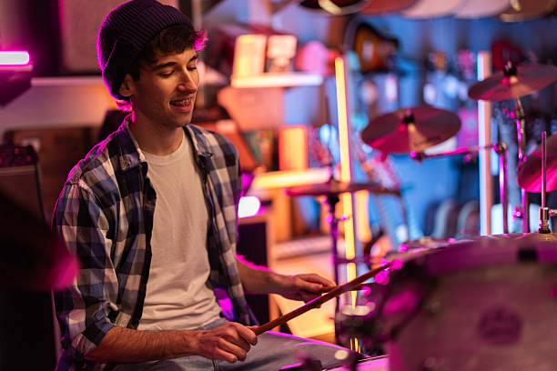 Smiling young man playing drums during rehearsal in neon lit studio