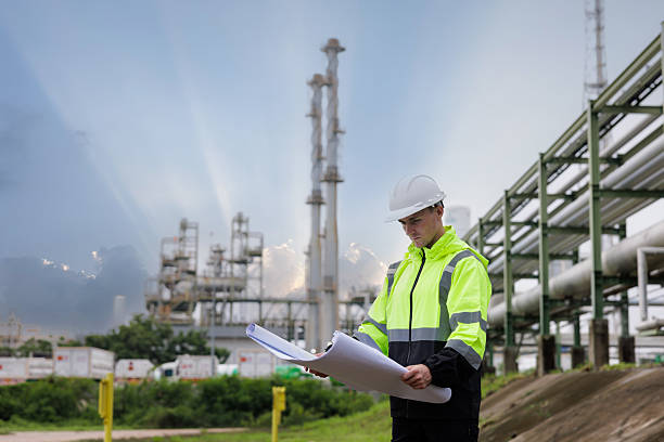istock engineer foreman wearing safety helmet holding and looking down at blueprint working in oil refinery industry plant background. 2211872421