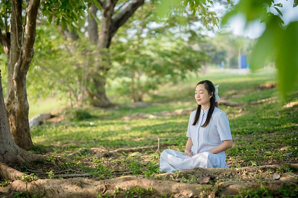 istock Asian woman meditating under green trees in peaceful park environment, practicing mindfulness and inner peace in natural setting with sunlight and serenity 2211879153