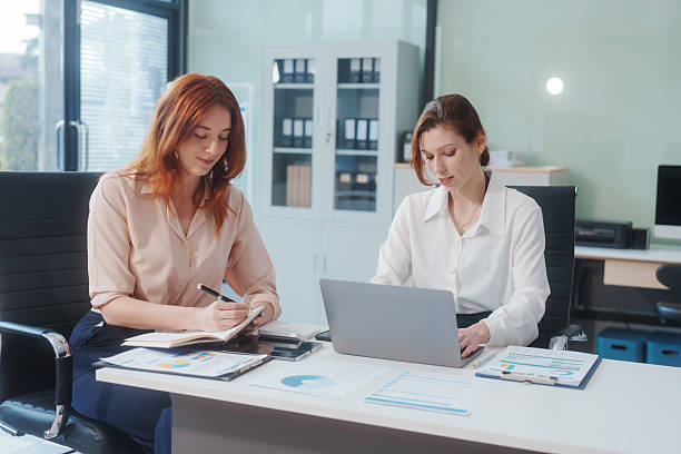 istock Two Caucasian women work in an office, happily using laptops and computers at a desk, discussing financial projects, analyzing financial statements,collaborating in a meeting to ensure effective 2211881417