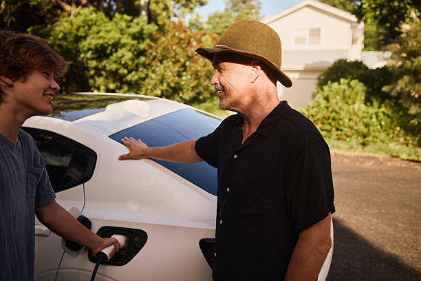 Father and son talking while charging their electric car in the driveway of their house