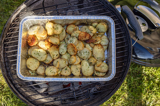 female hands cut bbq grill cooked potatoes and sausages in backyard in england uk.
