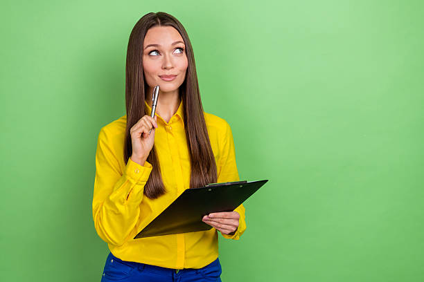istock Portrait of attractive cheerful bewildered girl writing plan deciding solution copy space isolated over green pastel color background 2211888700