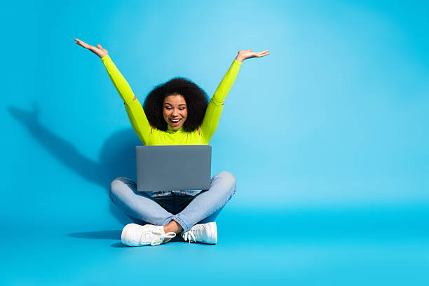 istock Cheerful young woman using laptop on blue background, celebrating success while enjoying online activities in a vibrant atmosphere 2211889750