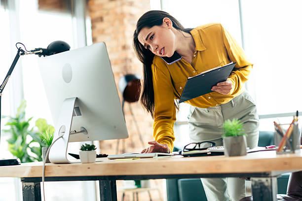 istock Focused businesswoman multitasking in a stylish office workspace with a computer and clipboard on a busy professional day. 2211890037