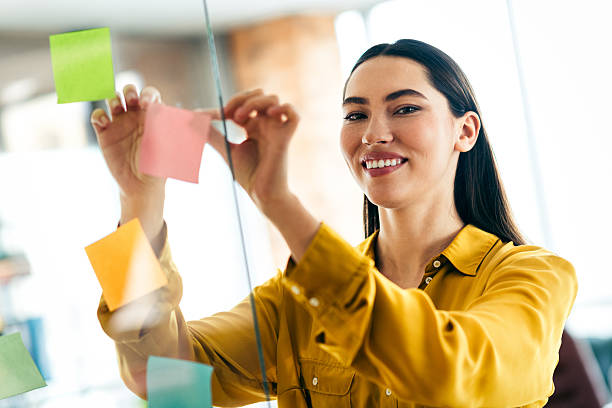 istock Young professional woman arranging colorful sticky notes in a modern office workspace, demonstrating creativity 2211890050