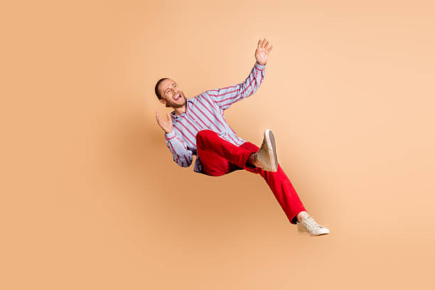 istock Young man in vibrant outfit making joyful gestures against a beige background, expressing happiness and energy in a candid moment 2211890489