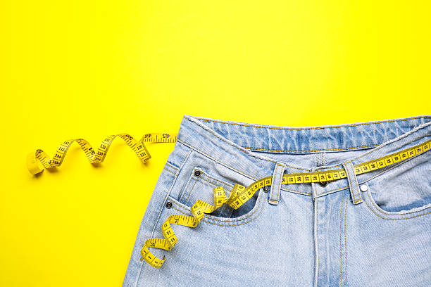 istock Jeans and measuring tape on yellow background, top view 2211892925