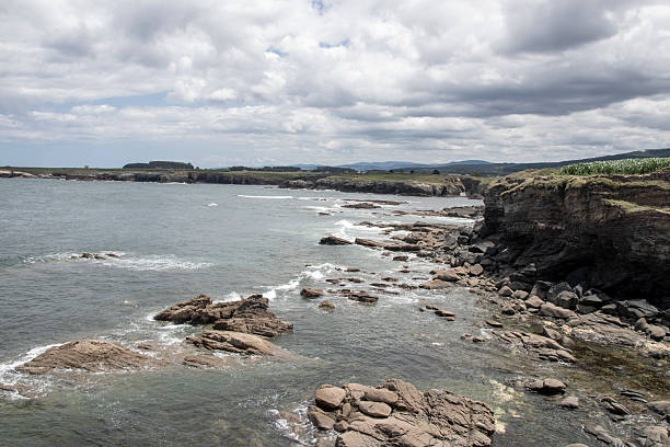 Scenic view of the rugged galician coastline with waves crashing against rocks under a cloudy sky