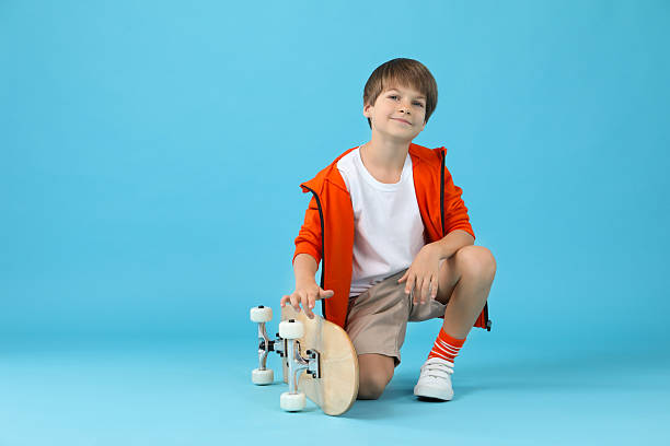 istock Little boy with skateboard on light blue background 2211893655