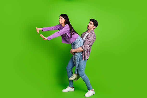 istock Young couple playfully interacting on a green background, showcasing a humorous and fun bond in casual outfits 2211894257