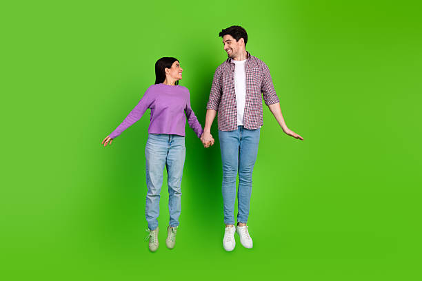 istock Young couple holding hands while smiling joyfully against a vibrant green background, showcasing positive emotions and togetherness 2211894314