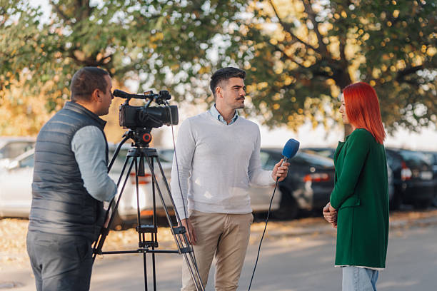 istock Journalist interviewing woman outdoors with cameraman filming 2211895086
