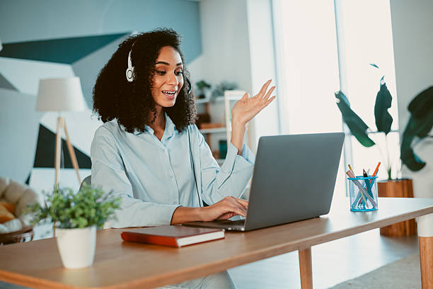istock Young woman in casual shirt using laptop and headset in modern home office during a virtual meeting 2211895607