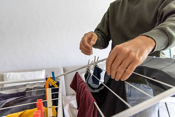 Close-up of hands hanging laundry on a drying rack. Domestic chore of air drying clothes indoors. Sustainable home living practice for energy conservation.