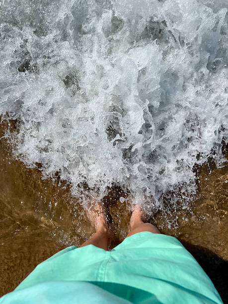 Tourist standing on the beach with sea waves washing over feet